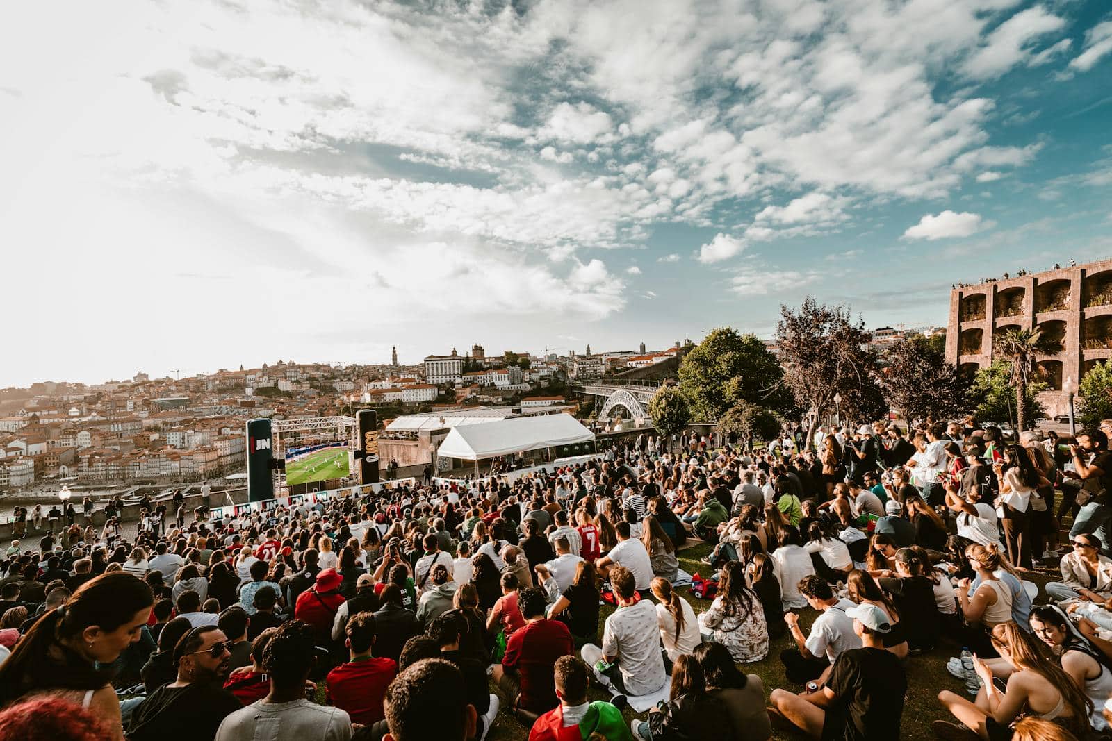 Fans gathered outdoors watching a football match on a giant public screen